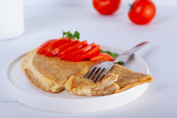 Oatmeal pancake with melted cheese and red tomato on white wooden background. Easy and quick breakfast.