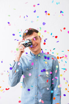 Smiling man taking a photo with an old camera as confetti falls from above.