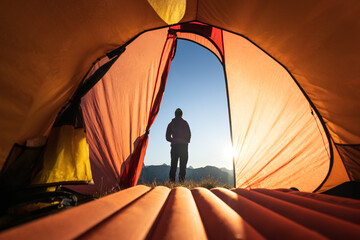 A woman looking at the sunrise in front of her tent in the mountains. © sanderstock