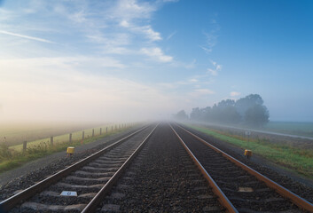 Fototapeta premium Empty railroad tracks disappearing into the spring fog.