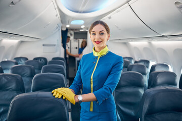 Young beautiful stewardess standing in the aisle of salon passenger airplane