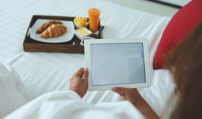 Faceless person browsing tablet while chilling on bed