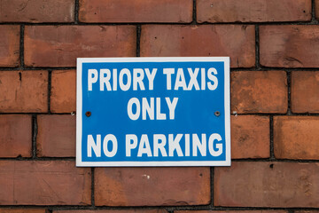 Blue and white taxi only no parking sign on brick wall