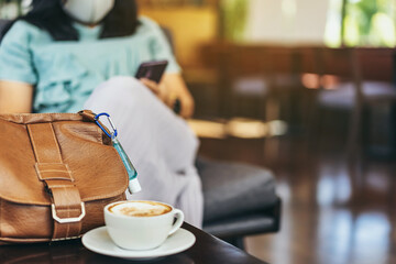 Mini alcohol gel bottle to kill Corona Virus(Covid-19) hang on a brown leather shoulder bag with hot coffee on table in cafe.New normal lifestyle.Health care concept.Selective focus on alcohol gel