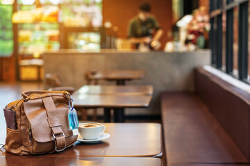 Mini alcohol gel bottle to kill Corona Virus(Covid-19) hang on a brown leather shoulder bag with hot coffee on table in cafe.New normal lifestyle.Health care concept.Selective focus on alcohol gel