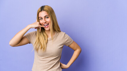 Young blonde woman isolated on purple background showing a mobile phone call gesture with fingers.