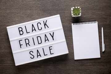 Black friday sale message on lightbox on a wooden desk.  Blank notepad for text.