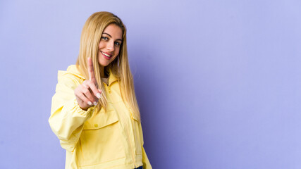 Young blonde woman isolated on purple background showing number one with finger.