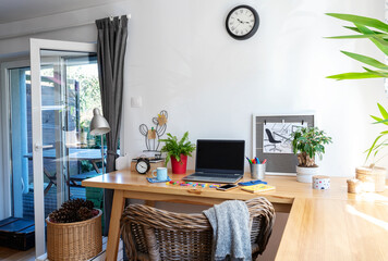 Interior of room with wooden office desk with laptop, green plants and coffee near window. Business and technology with white wall with copy space. 
