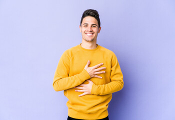 Young caucasian man isolated on purple background laughs happily and has fun keeping hands on...