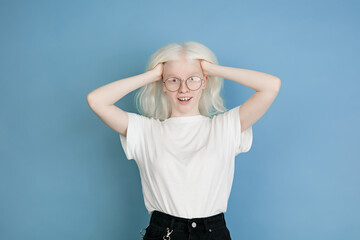 Angel's look. Close up portrait of beautiful caucasian albino girl isolated on blue. Blonde female model with stylish look. Concept of facial expression, human emotions, childhood, ad, sales