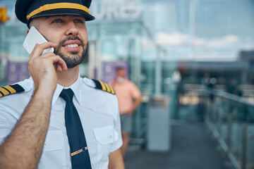 Cheerful male pilot talking on cellphone at airport