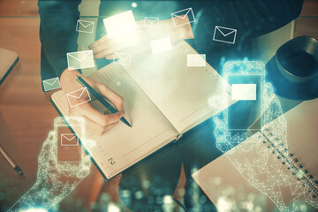 E-mail envelop theme hologram over hands taking notes background. Concept of electronic mail. Double exposure