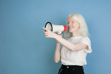Shouting with megaphone. Close up portrait of beautiful caucasian albino girl on blue. Blonde...