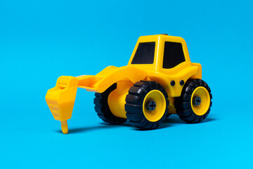 Children's toy yellow tractor truck drill on a blue background. Plastic construction equipment, toy store.