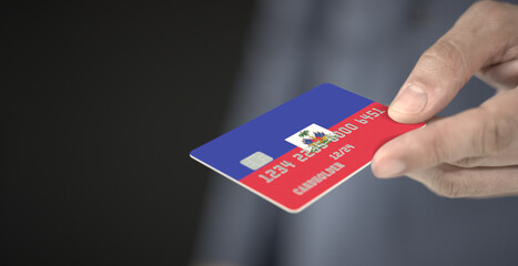 Man gives credit card with printed flag of Haiti. Fictional numbers