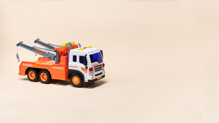 Toy orange tow truck on beige background banner with space for text. Children's car for loading and transporting cars.