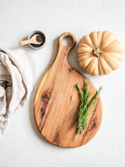 Food cooking concept. Beige pumpkin, wood cutting board for menu or recipe and fresh rosemary branches on the kitchen table. Top view. Copy space.