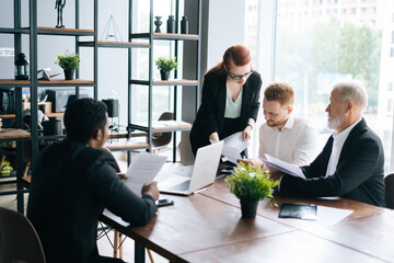 Young mixed race employees listening to confident female team leader. Business team of dedicated multi-ethnic of businesspeople discussing project while working together desk in office.