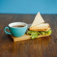 Cup of aromatic coffee placed on wooden table with tasty sandwich filled with ham and fresh lettuce
