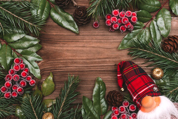 Christmas frame made of fir tree and magonia branches,cones,viburnum berries and toy gnome on the dark wooden rustic background.Christmas background.Copy space for text, top view.