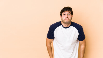 Young man isolated on beige background shrugs shoulders and open eyes confused.