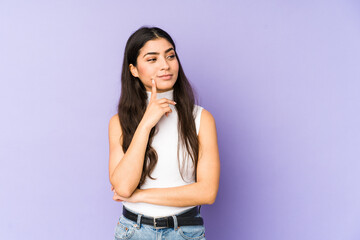 Young indian woman isolated on purple background contemplating, planning a strategy, thinking about the way of a business.