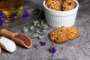 Closeup of multi grain cookies and hot english tea in luxury glass with saucer on gray table with dried flowers decoration.
