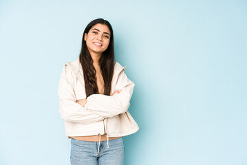 Young indian woman on blue background who feels confident, crossing arms with determination.