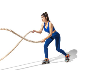 Ropes. Beautiful young female athlete practicing on white studio background, portrait with shadows. Sportive fit model in motion and action. Body building, healthy lifestyle, style concept.