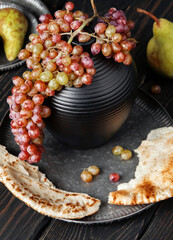 The vine hangs from a jug on a gray plate. Lavash is spread out on both sides of the plate. The black table creates perspective.