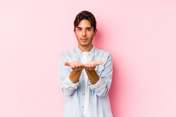 Young caucasian man posing in a pink background isolated holding something with palms, offering to camera.