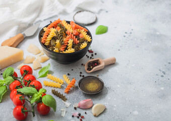 Fusilli pasta in black bowl with parmesan cheese and tomatoes, oil and garlic with basil and linen towel on light background.