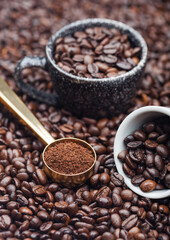 Fresh raw organic ground coffee powder in black steel scoop with blackand white cups on top of coffee beans.