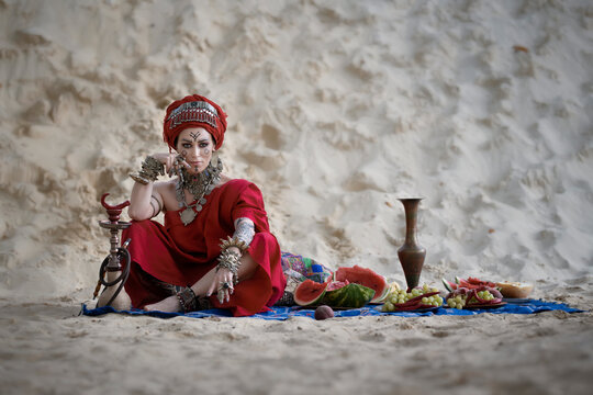 Berber woman in red clothes on a carpet among the sand