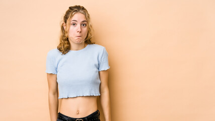 Young caucasian woman isolated on beige background shrugs shoulders and open eyes confused.