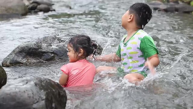 Two asian children playing water in the river in a mountainous area