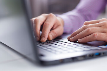 Male executive hands typing and scrolling on a laptop computer device with blur background. Working online from home. 
