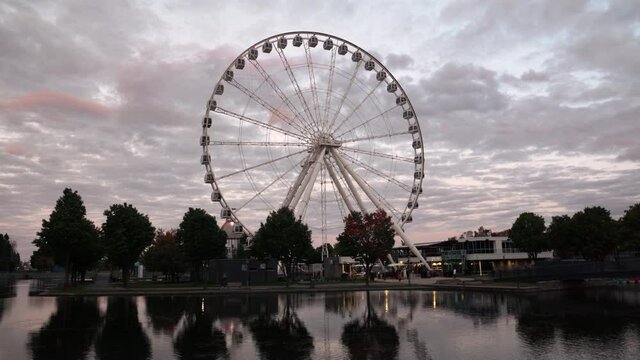 Grande roue de Montreal - Ferris Wheel Spinning With Reflection On The Water During Sunset At The Old Port Of Montreal In Quebec, Canada  - Coronavirus Pandemic Outbreak. - wide shot
