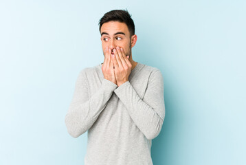 Young caucasian man isolated on blue background thoughtful looking to a copy space covering mouth with hand.