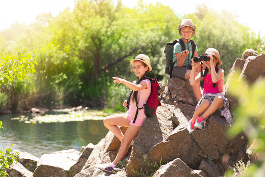 School holidays. Group of happy children sitting on rocks near river