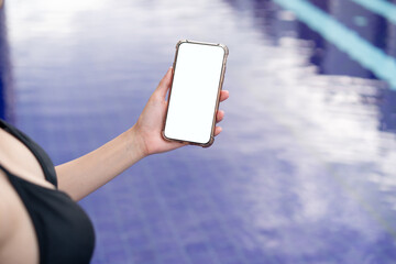 Woman hand holding mobile phone with blank white screen mockup by the pool.