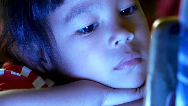 Close up of little girl in bed looking at the smartphone at night and the blue light has a negative effect on children's eyes.