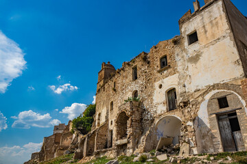 Fototapeta premium Craco, Basilicata, Italy. Ghost town destroyed and abandoned following a landslide. Collapsed houses and the remains invaded by vegetation. Broken walls, windows and doors. Bell tower of the church