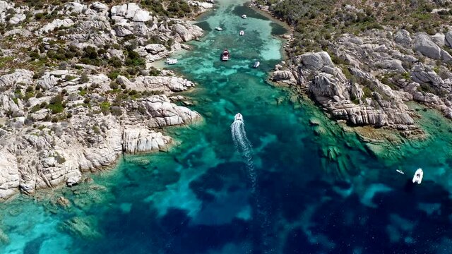 Boat Entering Small Private Cala at Caprera Island, Sardinia, Italy.
Aerial Drone View. Rocky Coastline. Turquoise Cristal Clear Sea.