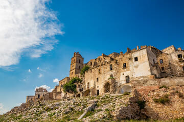 Fototapeta na wymiar Craco, Basilicata, Italy. Ghost town destroyed and abandoned following a landslide. Collapsed houses and the remains invaded by vegetation. Broken walls, windows and doors. Bell tower of the church