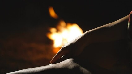 Attractive woman sitting and gently stroking her slim leg with bright fire at background. Sexy girl enjoying calm scene with warm bonfire. Young lady having leisure at night outdoor. Blurred backdrop