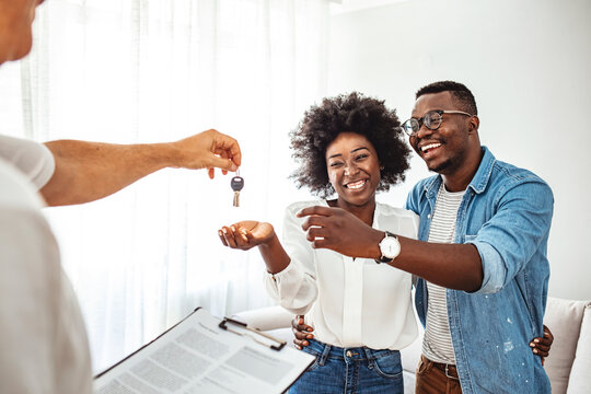 Happy couple is taking keys from their new house from broker and smiling. Hands of estate agent giving keys to the couple. The agent handed the keys a young couple