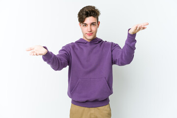 Fototapeta premium Young caucasian man isolated on white background makes scale with arms, feels happy and confident.
