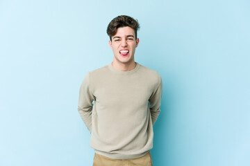 Young caucasian man isolated on blue background funny and friendly sticking out tongue.